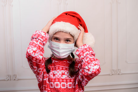 Fun little girl wearing a Santa hat and a medical mask. Child girl with happy expression on christmas day.の写真素材