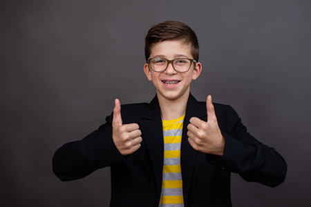 happy funny boy with glasses show a thumbs up and good luck. on a black, dark gray background.の写真素材