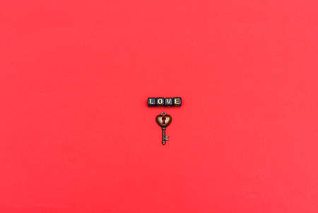 The inscription love is laid out with cubes with letters and a metal key in the form of a heart on a red background.の写真素材