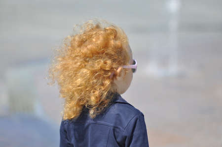 A red-haired girl with flying hair on a sunny day on the street.の写真素材