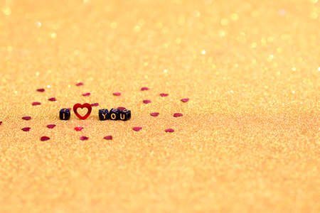 The inscription I love you is written on cubes with red hearts on a gold background. Bokeh and selective defocusing.の写真素材