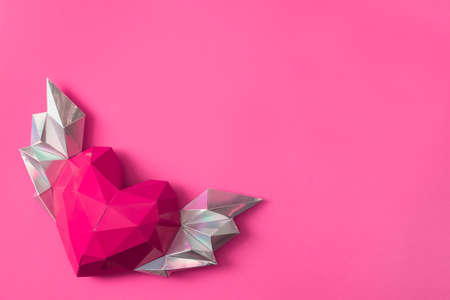 Pink polygonal paper heart with wings on a pink background.の写真素材