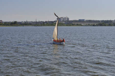 Small sailboat in a calm lake on the background of a large city.の写真素材