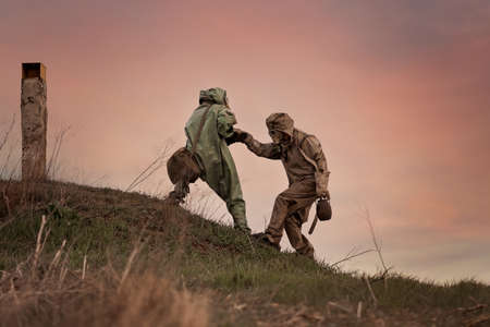 A man in a gas mask and a chemical protection suit helps another person to walk. Post-apocalypse after nuclear war and radiation pollution.の写真素材