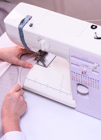 Female hands stitching light fabric on machine.