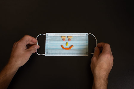 Medical mask in the hands of men. A protective mask with a smiley face made of tablets.