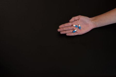 Pills in the hand of a teenage girl on a black background