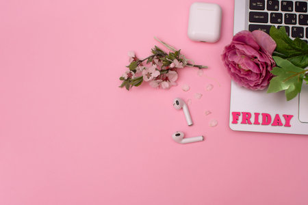 top view. lettering friday. headphones, a blooming twig, a laptop, a rose flower. on a pink...