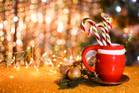 red cup on a saucer with candy cane, Christmas toys, with lights on a golden bokeh background. copy space. christmas card background.の写真素材