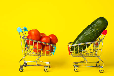 tomatoes and cucumbers in shopping baskets. on a yellow background. copy spaceの写真素材