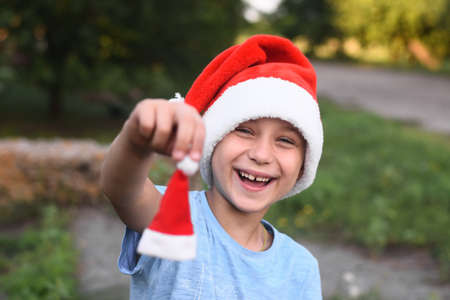 a laughing boy in a Santa hat holds a small Santa helper hat in his hand.の写真素材