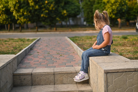 A little girl sits on a step outside and looks into the distanceの写真素材