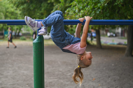 active recreation of a little girl. The child is hanging upside down on the bars