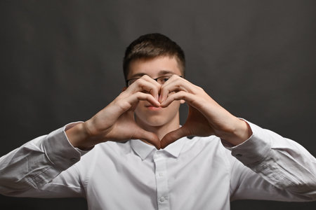 Young man wearing white t shirt smiling doing heart symbol shape with hands. romantic love concept.