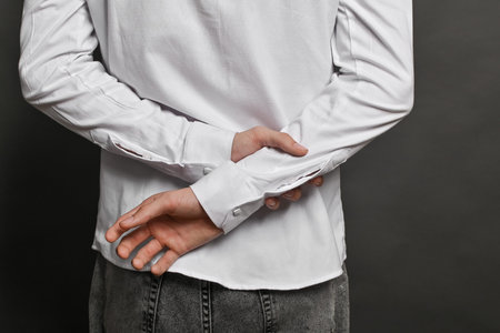 A mans hands clasped behind his back. He wrapped his hand around the wrist of his other hand.