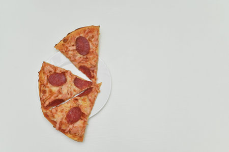 slices of pepperoni pizza arranged on white plate, isolated on white background. pizza shows golden...