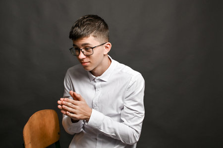 young man sits with hands rubbing together, gesture often expressing anticipation, anxiety, or inner...