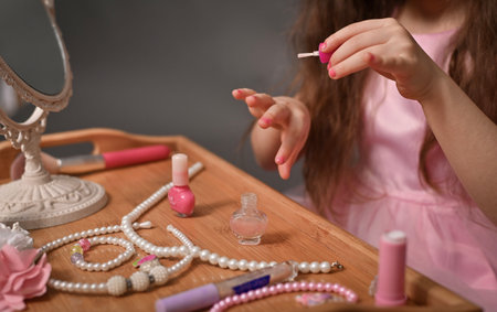 Hands of little girl performing manicure with nail polish surrounded by pearls and decorations, symbolizing beauty. child painting nails. fashion and beauty for children conceptの写真素材