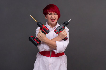 Power tool demonstration by skilled female worker. Neutral background focuses attention on drill features and user's technical posture. makes this ideal for tool advertisements or manuals.の写真素材