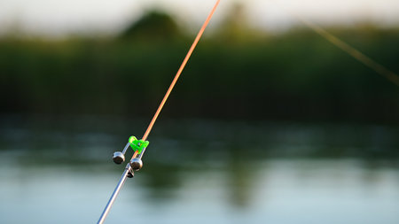 There is a warning bell on the edge of the fishing rod, signaling a bite. a fishing scene.の写真素材
