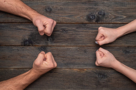 People hands forming tight fists arranged opposite on rustic wooden background, male and female hands symbolizing challenge, resistance and force. man and woman conflict concept, strength, rivalry,の写真素材
