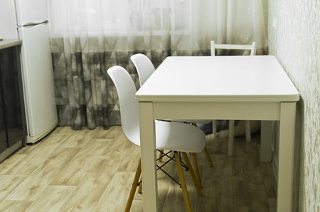 Table placed in modern dining room with white chairs on wooden floor. Table stands near window with...