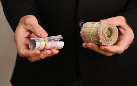 Money rolls in hands of businessman dressed in dark jacket, cash bundles rolled and held in palms....