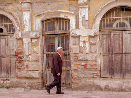 Albania, Shkoder- July, 2016 An elderly man taking a walk, passing by a slightly ruined houseのeditorial素材