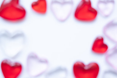 Blurred Valentine`s day background with hearts. Copy space. Shiny glass hearts on white background.