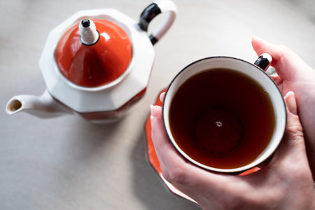 Hands holding a teacup. Relaxing teatime. Black tea in beautiful old Langebraun red porcelain tea set called "Muhu mÃ¤nd".の写真素材