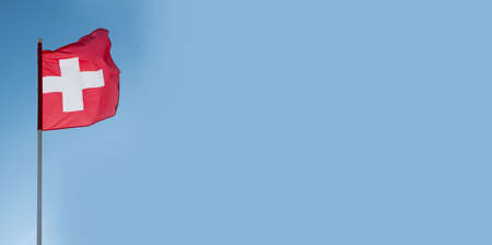 Swiss flag waving in wind. Flag of Switzerland on blue sky background. Empty copy space.の写真素材