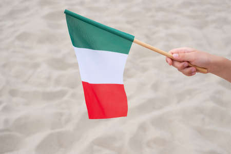 Child's hand waving Italian flag. Small flag of Italy on sand background. Empty copy space.の写真素材