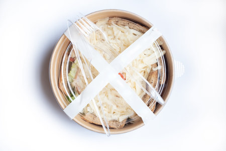 Caesar salad with chicken fillet in a take-away box isolated on white background. Delicious fresh chicken salad in a round brown food container with plastic knife and fork.の写真素材