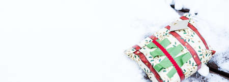 Christmas gift in snow. Horizontal banner with empty copy space. Beautifully wrapped Christmas present laying outdoors in natural environment during winter, holiday season.の写真素材