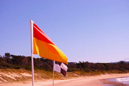Beach flags on Australian beach. Red and yellow flag. Black and white flag. Lifesaver signs. Lifeguard flags on seashore at Coffs Harbour, Australia.の写真素材