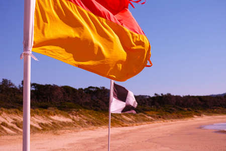 Beach flags on Australian beach. Red and yellow flag. Black and white flag. Lifesaver signs. Lifeguard flags on seashore at Coffs Harbour, Australia.の写真素材