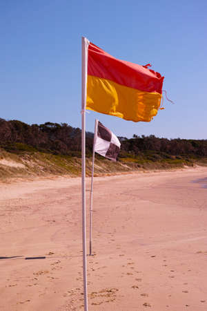 Beach flags on Australian beach. Red and yellow flag. Black and white flag. Lifesaver signs. Lifeguard flags on seashore at Coffs Harbour, Australia.の写真素材