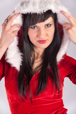 young beautiful Christmas woman, studio portrait Sexy Santa, grey background with long black hair and red haの写真素材