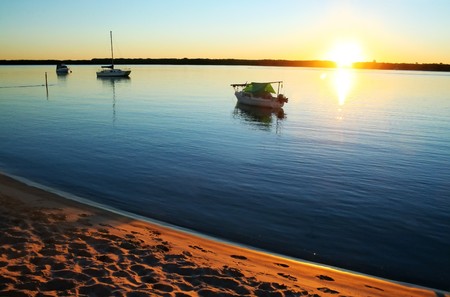 Sun streams over small boats in a still lagoon at dawn.の写真素材