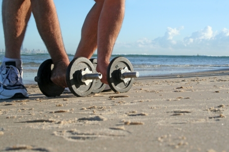 Man picks up work out weights on the beach at sunrise.の写真素材