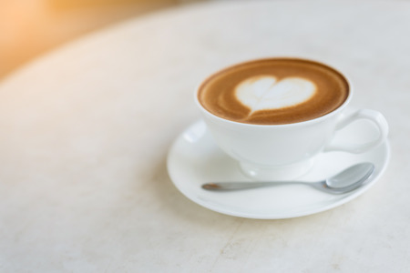 A cup of coffee with heart pattern in a white cup on wooden backgroundの写真素材