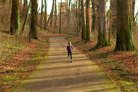 A rushing long-haired girl rides a scooter along the path in the park.