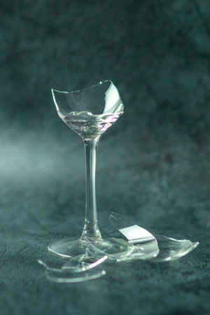 The lonely leg of a broken wine glass against a pale charcoal background together with pieces of...