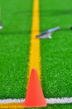 An orange cone marke the corner of the out of bound lines on a turf field with a lacrosse stick in the background.の写真素材