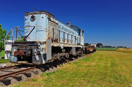 A retired diesel train engine sits on this side track under a clear blue sky on a hot summer day.