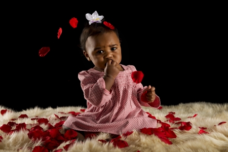 Beautiful baby girl with rose pedals and fur rugの写真素材