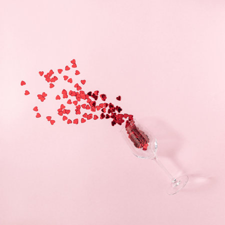 Transparent wine glass with spilled red hearts on bright pink background.  Creative minimal  flat lay concept.の写真素材