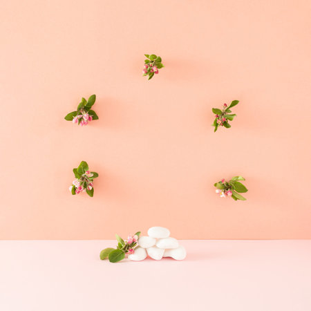 Creative showcase made with white rocks and blooming flowers against a pink and orange background....