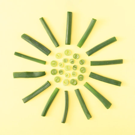 Sun-shaped arrangement of spring onion slices on bright yellow background. Creative food concept....