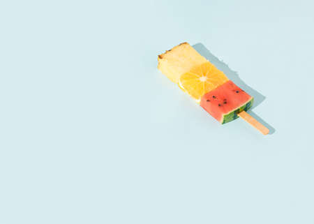 Colorful Ice cream made of watermelon, orange, and pineapple fruits slices with sunlight shadow on pastel blue background. Minimal summer concept. Creative food idea.の写真素材